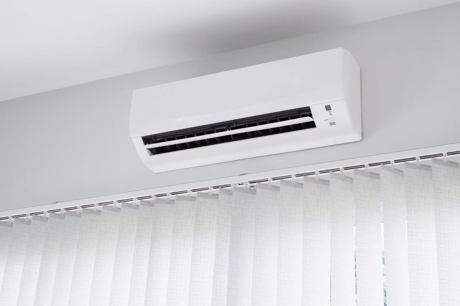 White wall-mounted air conditioner above vertical white blinds