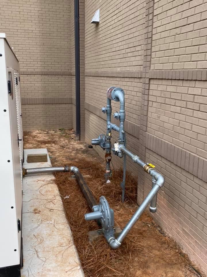 Gas pipes and regulators next to a building. Gray pipes run along the ground and up the wall.