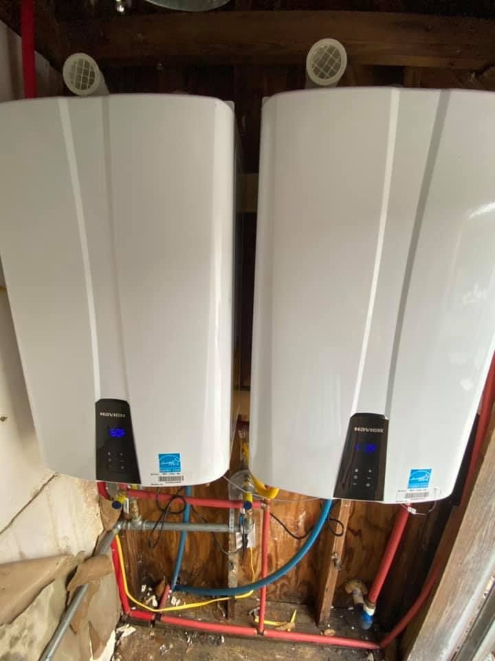 Two white water heaters mounted on a wall. Red and blue pipes connect to the units.
