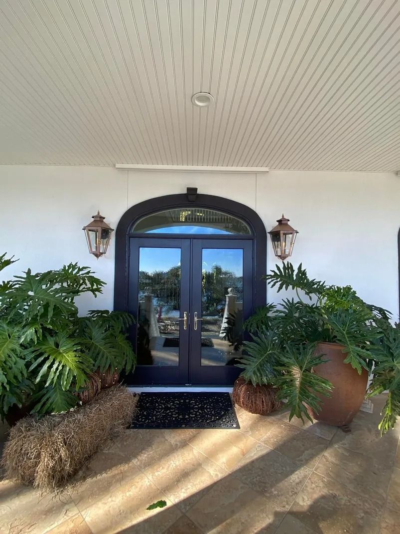 Black double doors with arched transom, flanked by potted plants, two sconces, and a large ceramic pot.