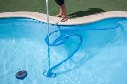 Person using a blue pool skimmer to remove debris from a swimming pool