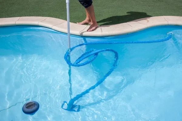 Person pulling a blue pool skimmer net through a swimming pool near the edge
