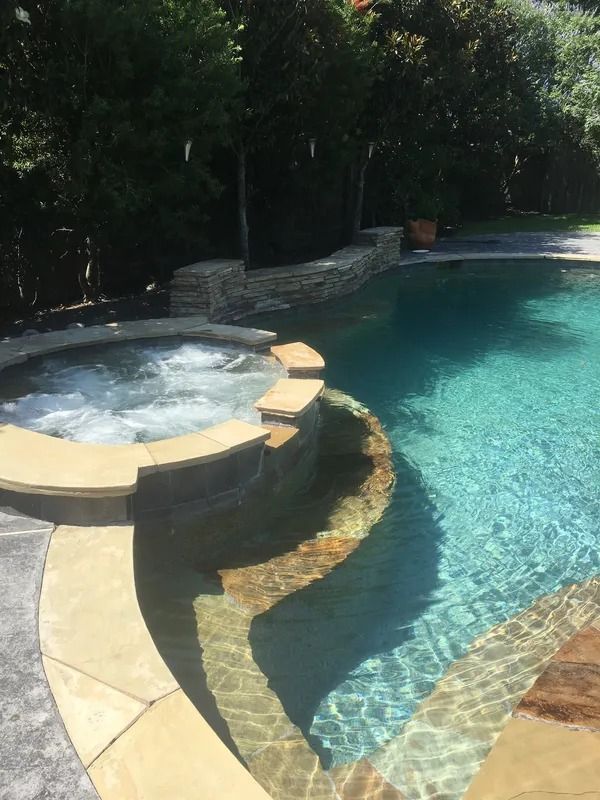 Backyard pool with a built-in hot tub, curved stone deck, and clear blue water