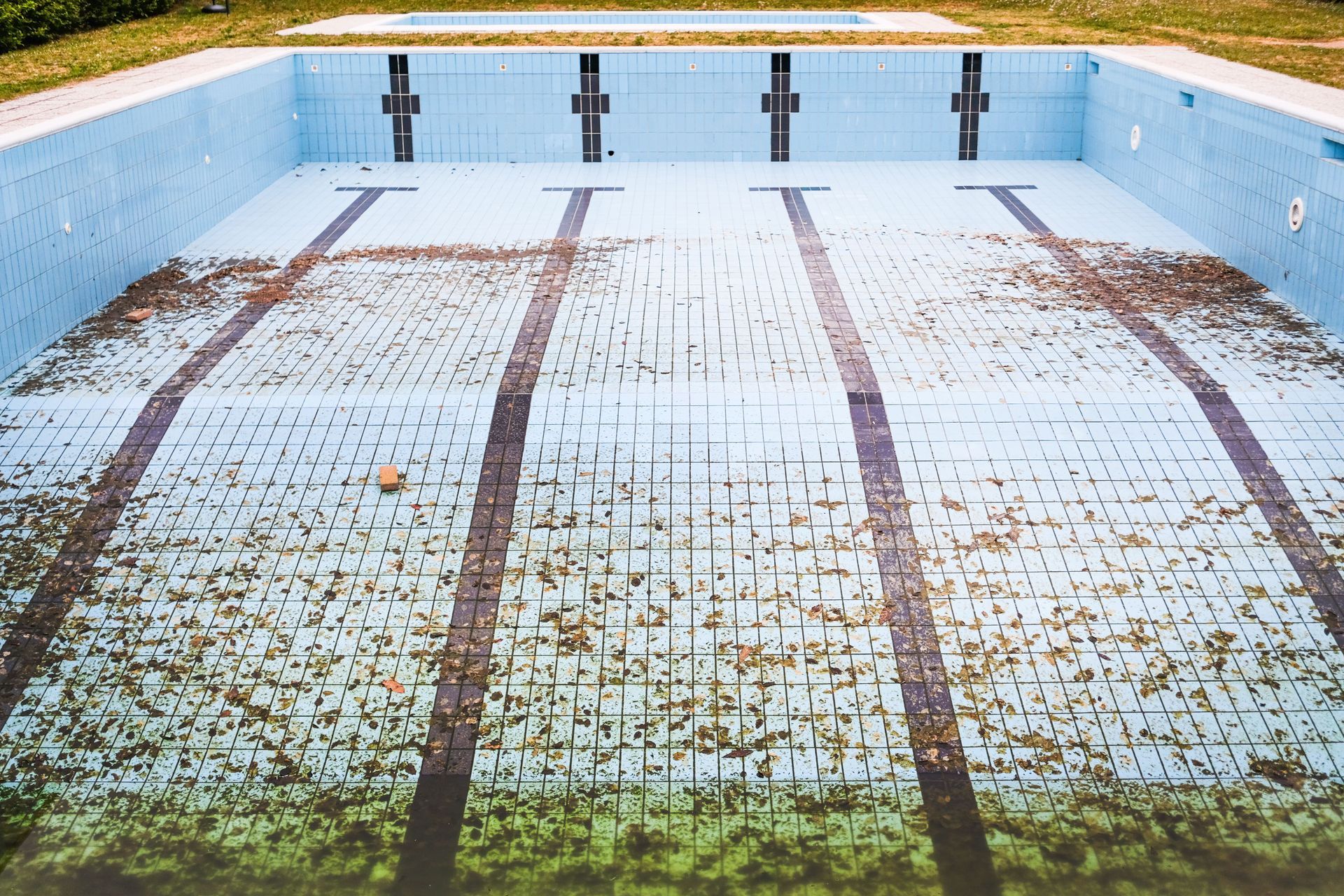 Empty, stained swimming pool with peeling white tiles and blue walls