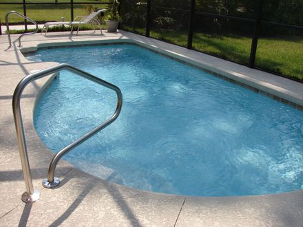 Backyard swimming pool with blue water and a metal handrail by a fenced deck