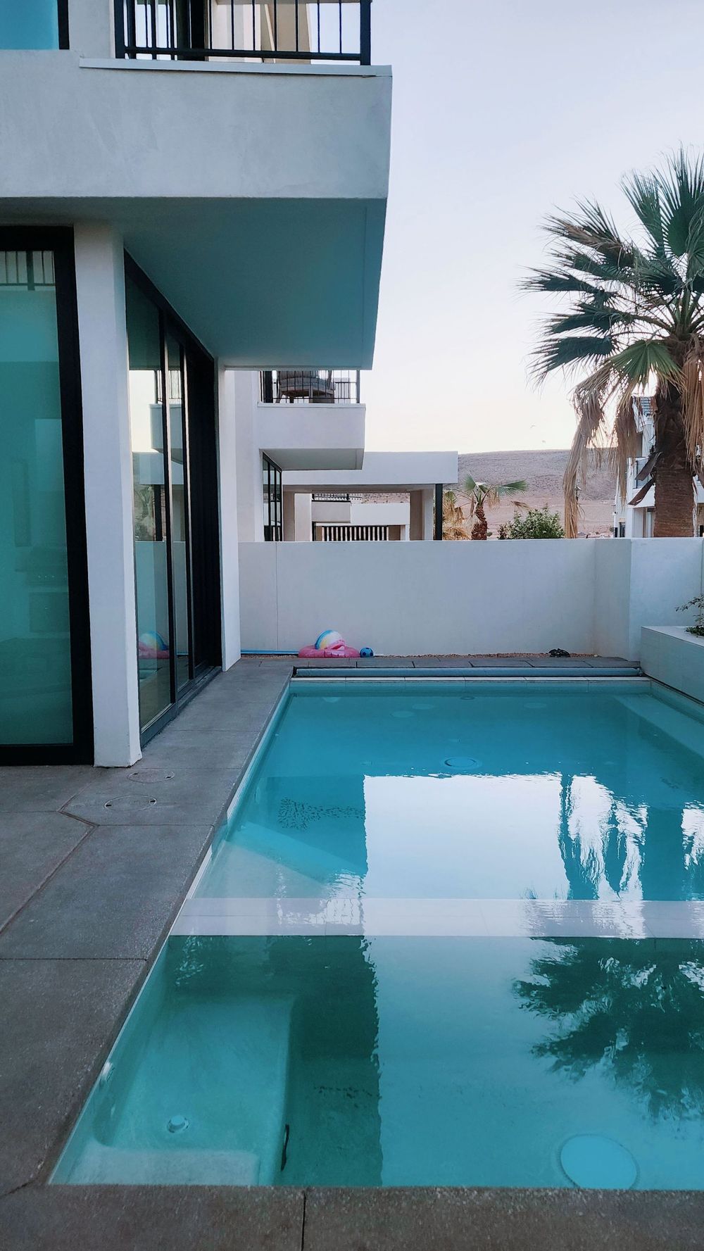 Modern patio with a small turquoise pool beside a white house and palm tree at sunset