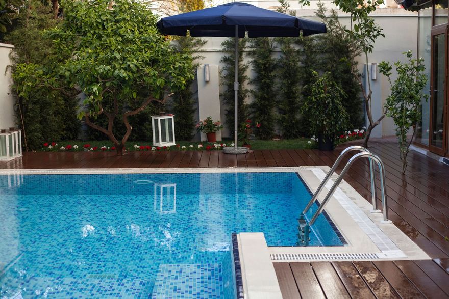 Backyard swimming pool with blue water, white lounge chairs, and a dark umbrella beside wooden decking