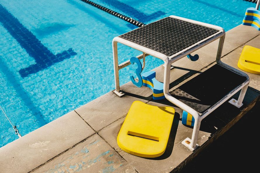 Pool lift chair beside a swimming pool, with a yellow seat at the water’s edge.
