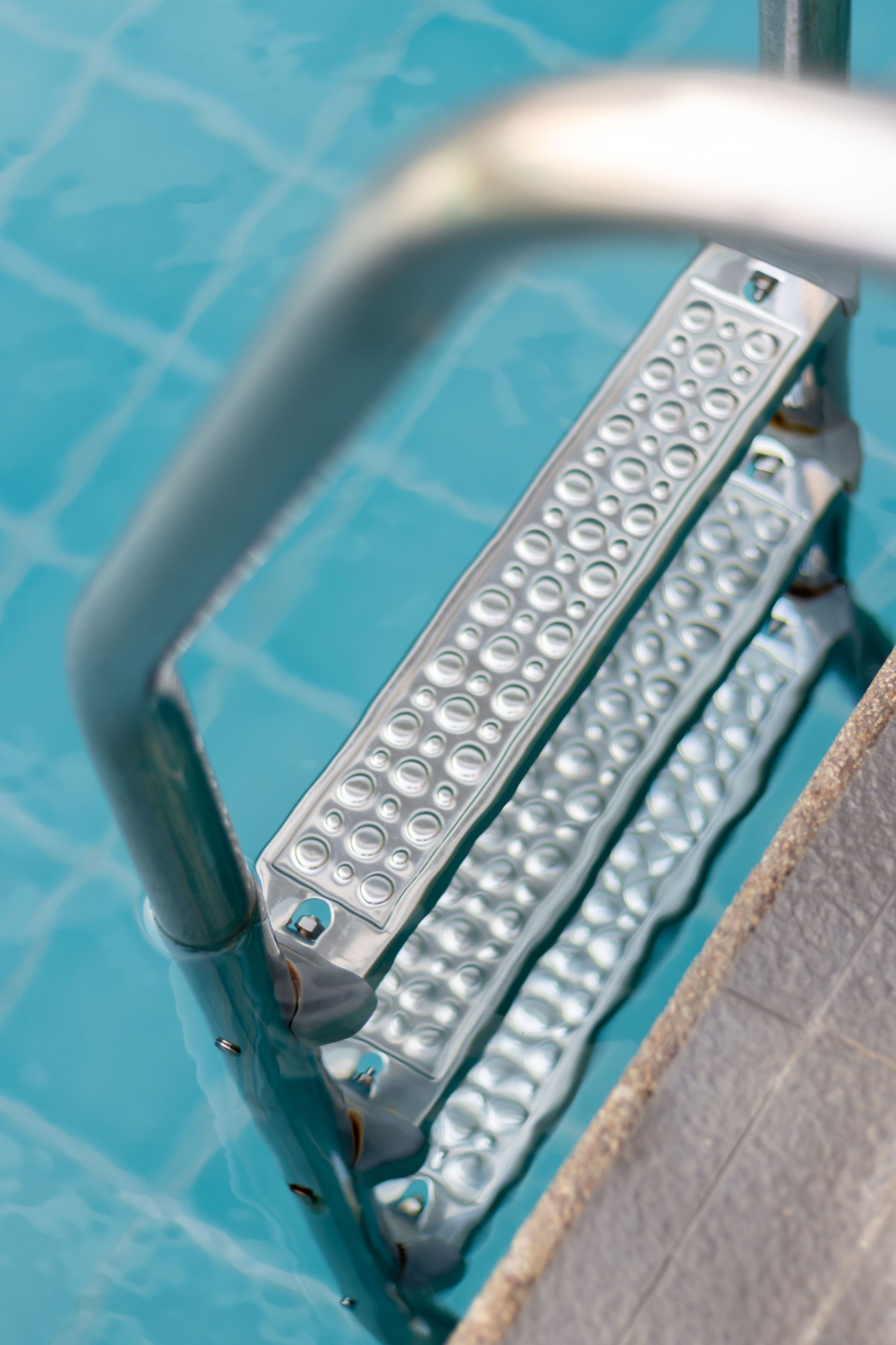 Close-up of a metal stair with a curved handrail over turquoise tile flooring