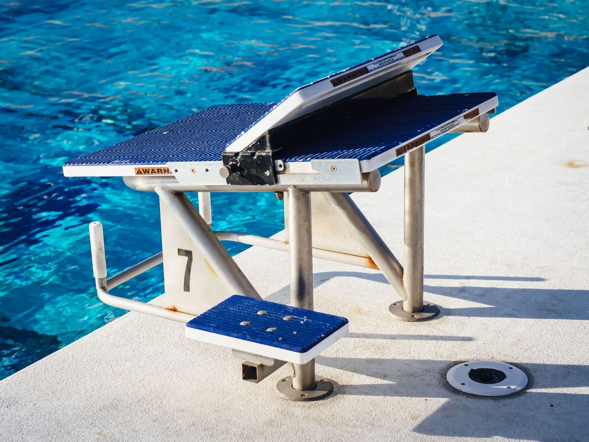Swimming pool diving platform with blue surface and white metal support ladder