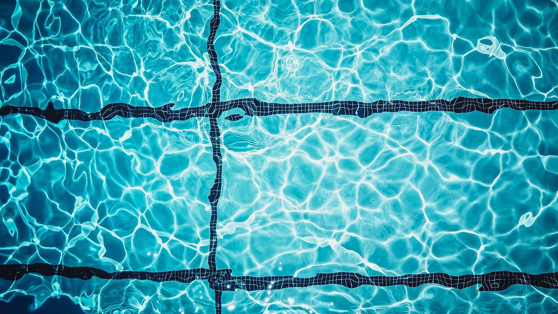Blue pool water with sunlight reflections and dark lane lines underwater