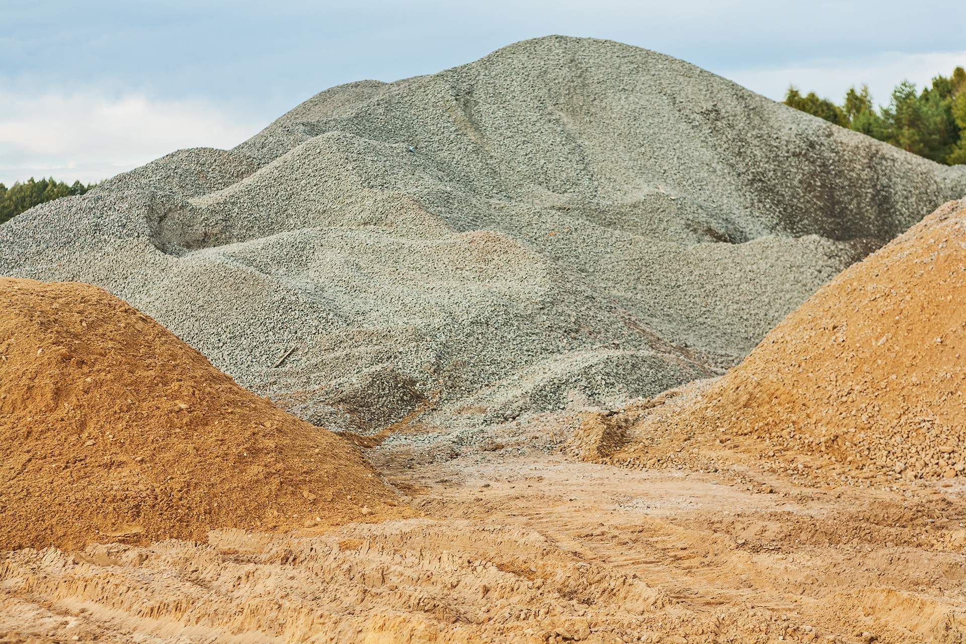 A pile of gravel and sand in a field with trees in the background.