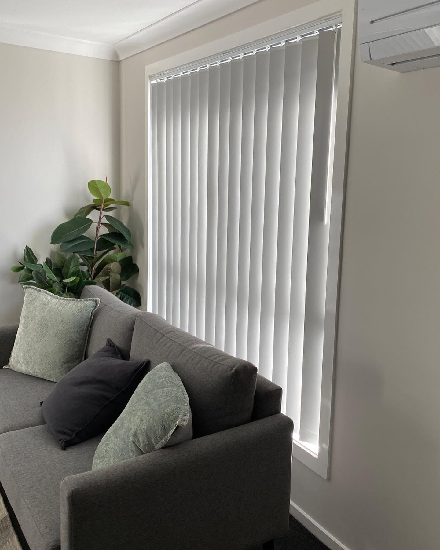 A Sofa With Pillows Beside a Window With Vertical Blinds — Douglass Blinds & Security Screens in Wagga Wagga, NSW