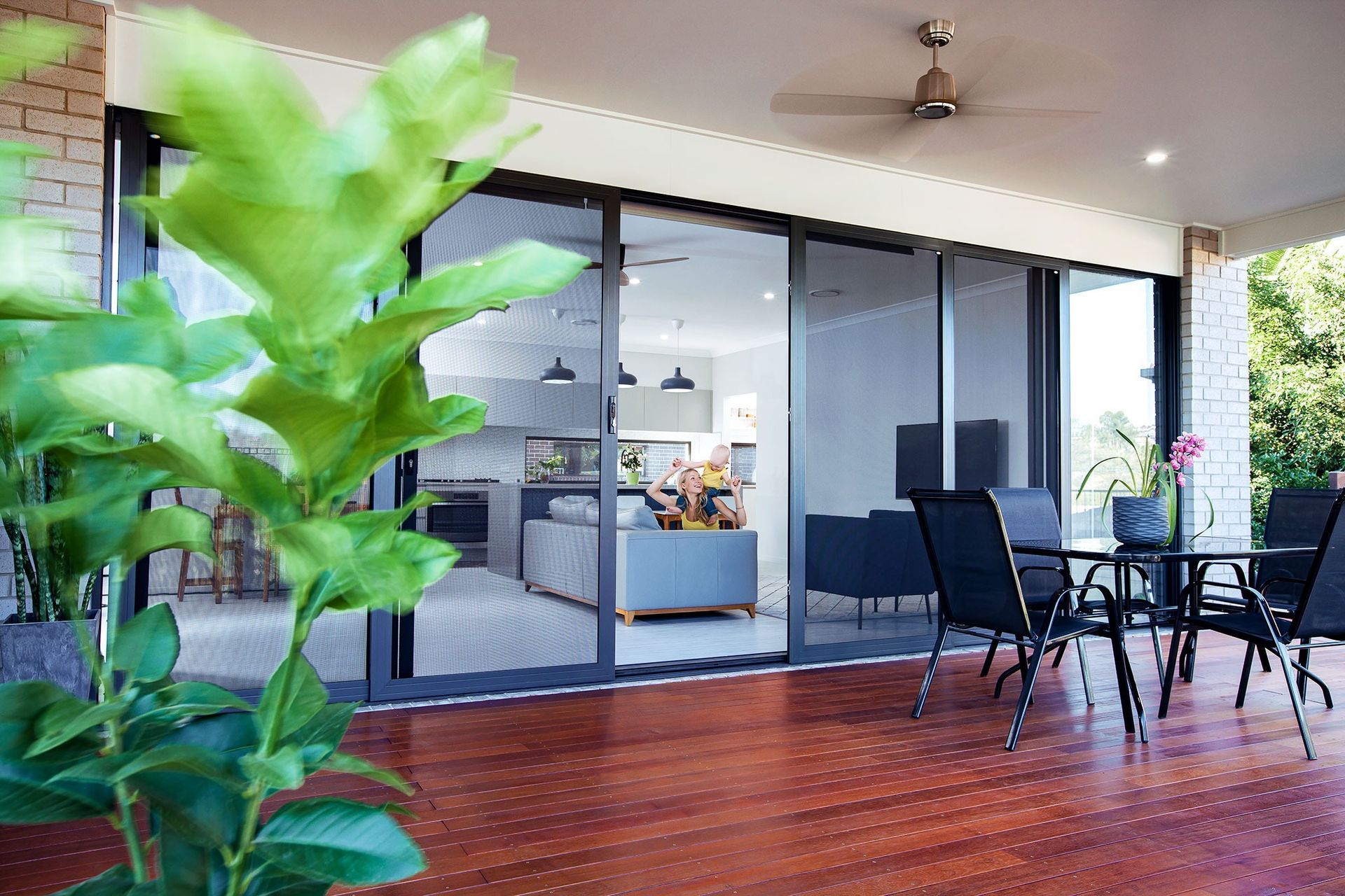 Covered patio with wooden deck, black outdoor dining set, sliding glass doors, and a potted plant in the foreground — Douglass Blinds & Security Screens in Wagga Wagga, NSW
