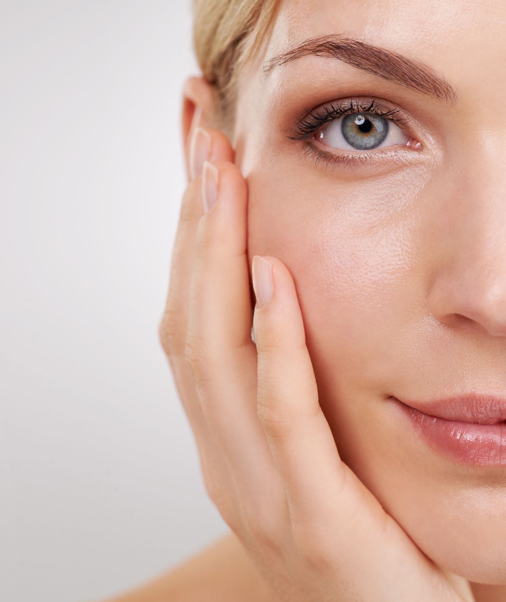 Woman's face, partially visible, touching cheek with hand, natural makeup, fair skin, light background.