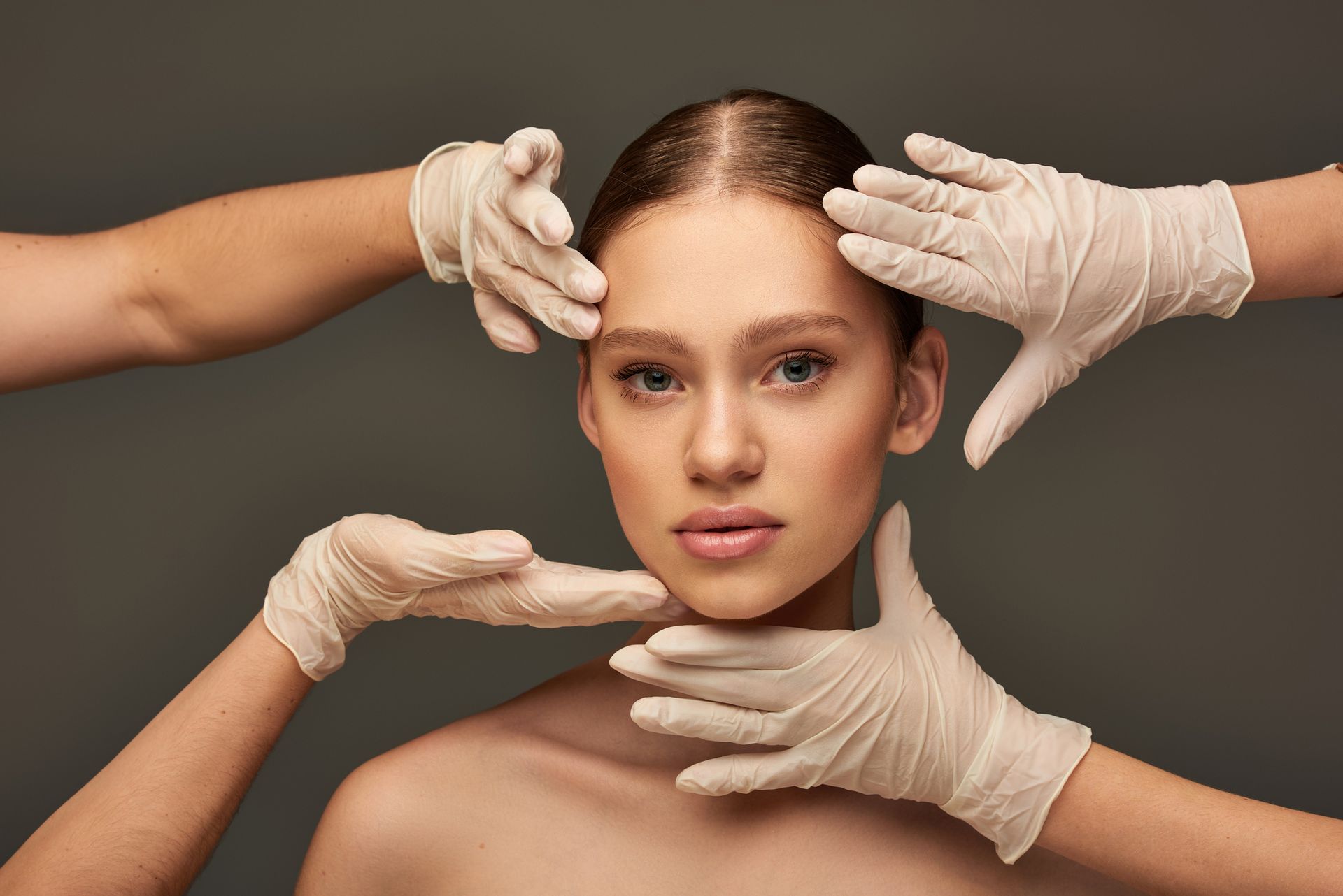 Woman’s face framed by gloved hands, dark background. Hands touch forehead, cheeks, and jaw.