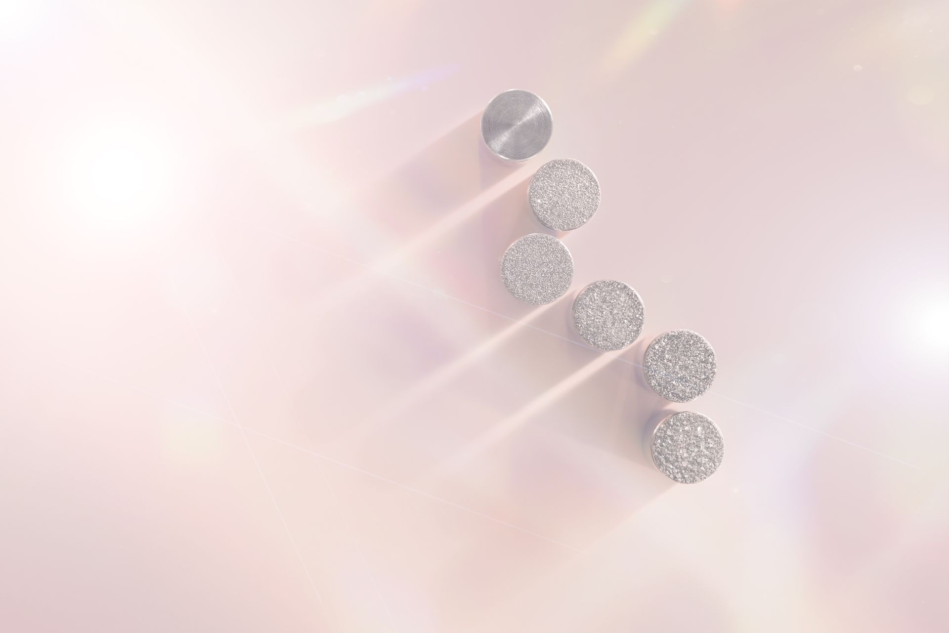 Silver studs and textured stones in a diagonal line on a pink surface with shadows and lens flares.