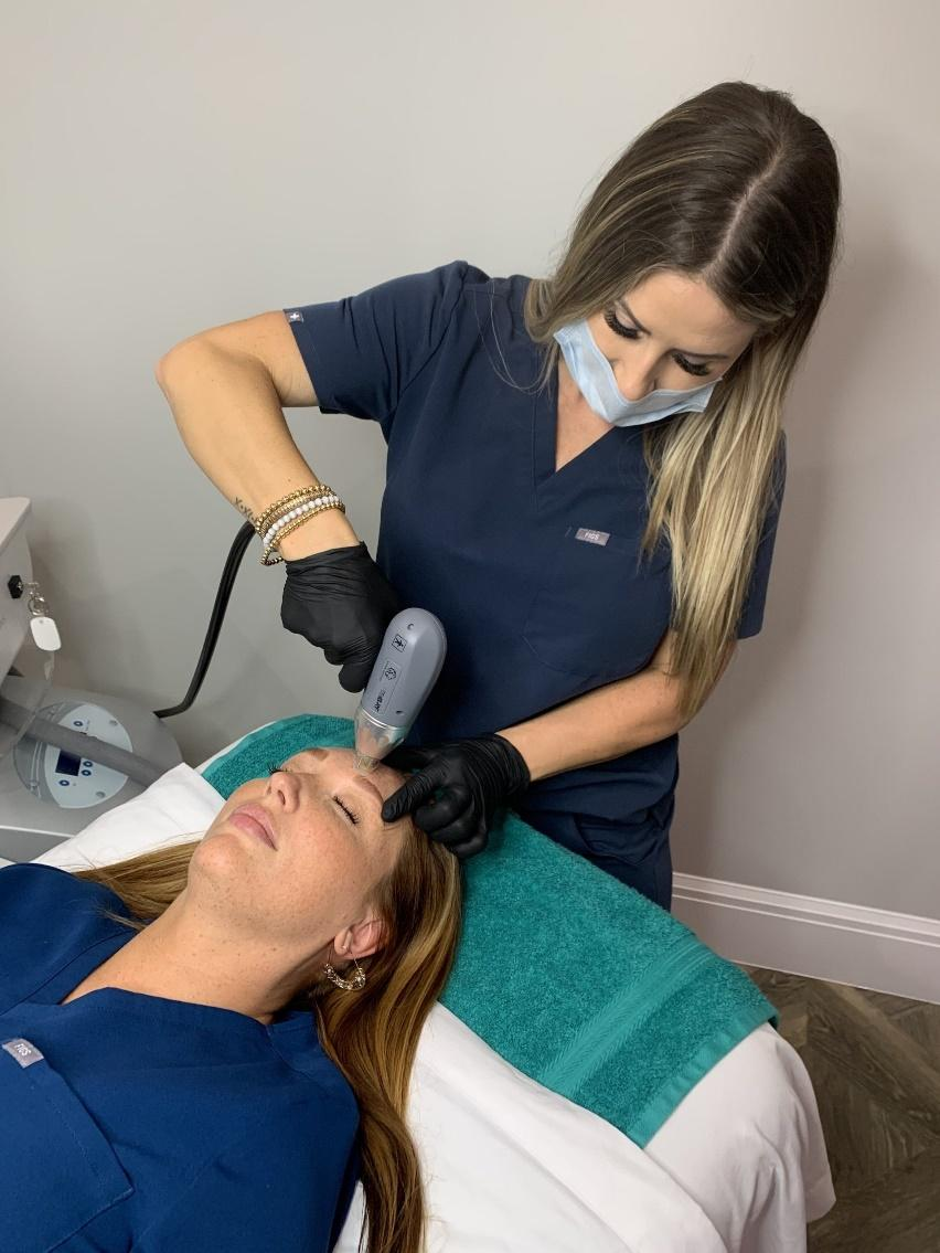 Woman receiving a skin treatment on her forehead. Technician in scrubs operates a device.