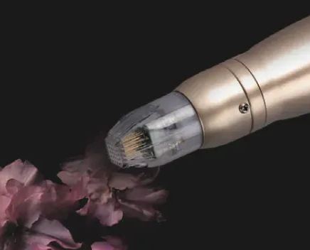 Close-up of a microneedling device with tiny needles, near pink flowers, on a dark background.