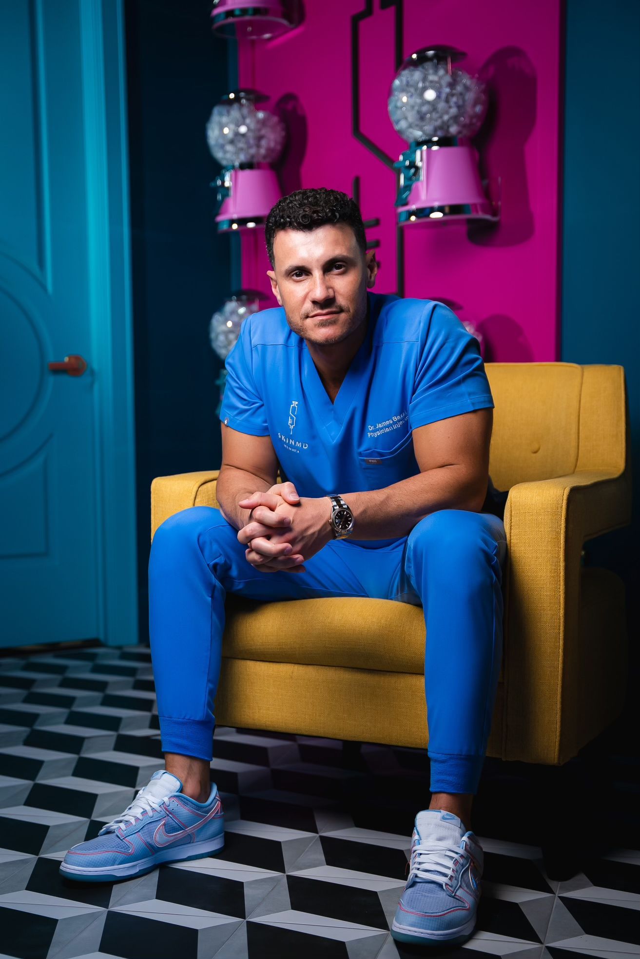 Dr. James Bazzi, MD, owner of SkinMD Michigan  on a yellow chair, in front of a pink wall with gumball machines.
