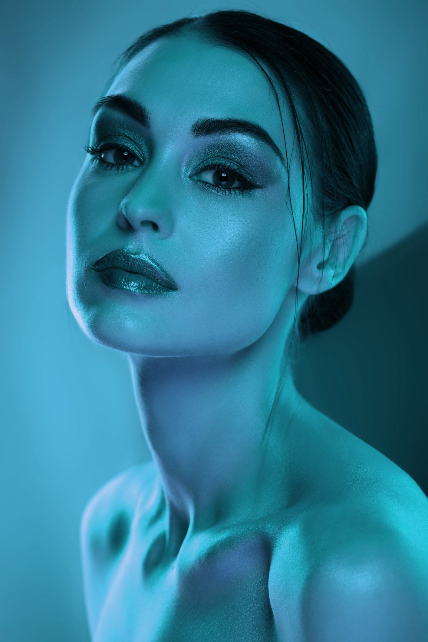 Woman with shimmering makeup, bathed in blue light, gazing at the camera.