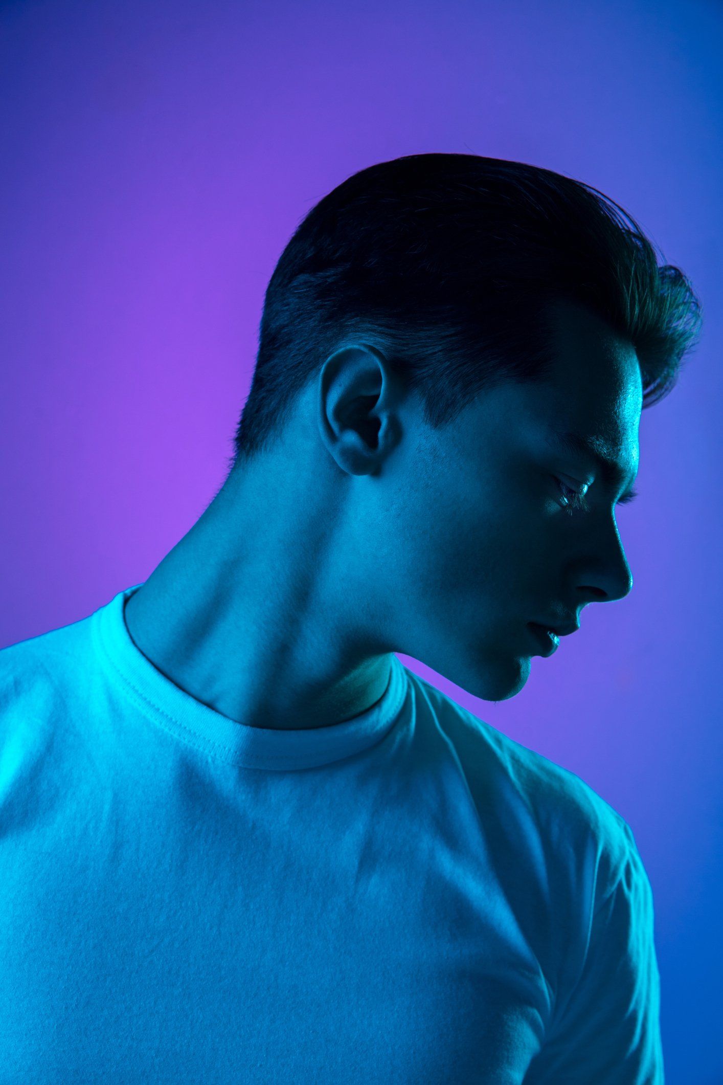 Man in a white shirt, lit by blue and purple light, looking down.