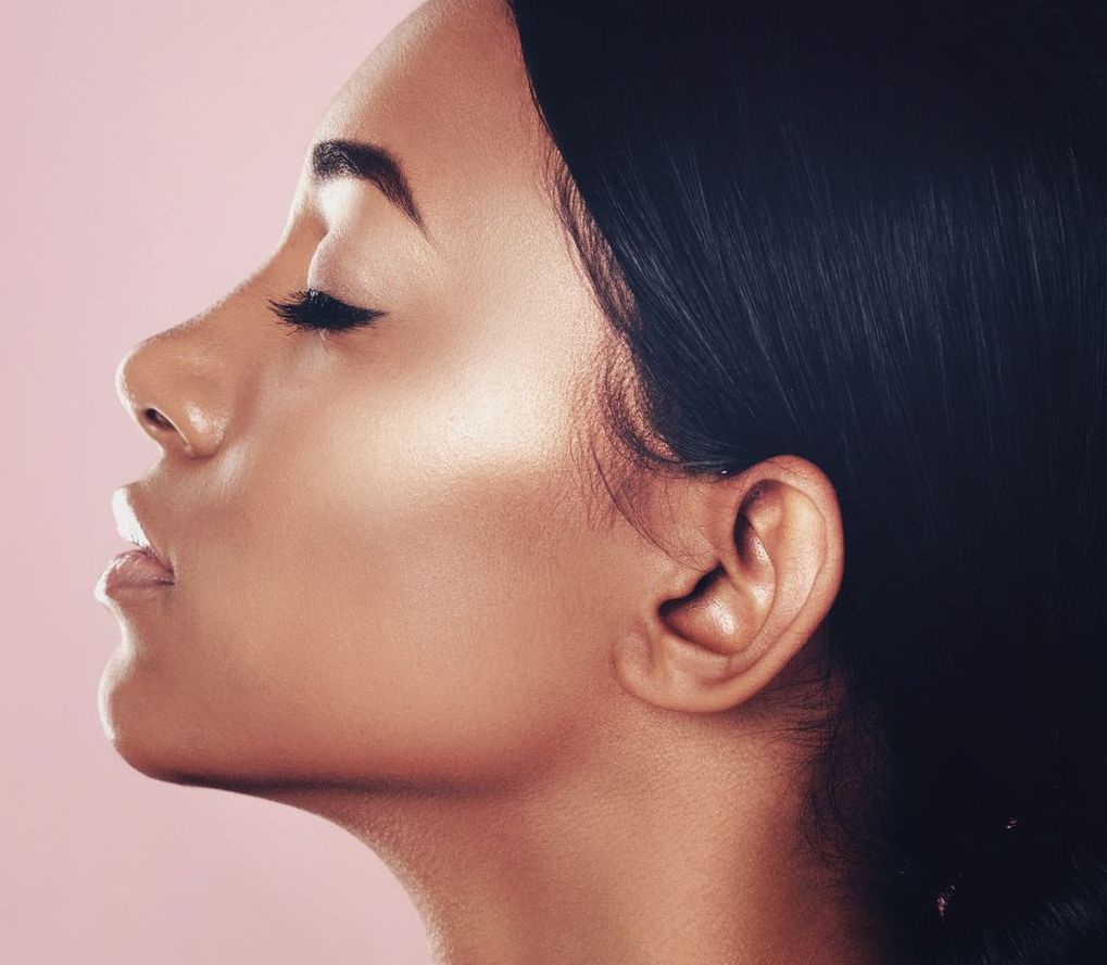 Profile of a person with closed eyes, smooth skin, and dark hair against a pink background.