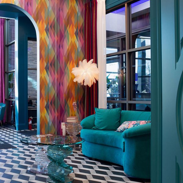 Colorful living room: teal couch, patterned wallpaper, black and white checkered floor, arched doorway.