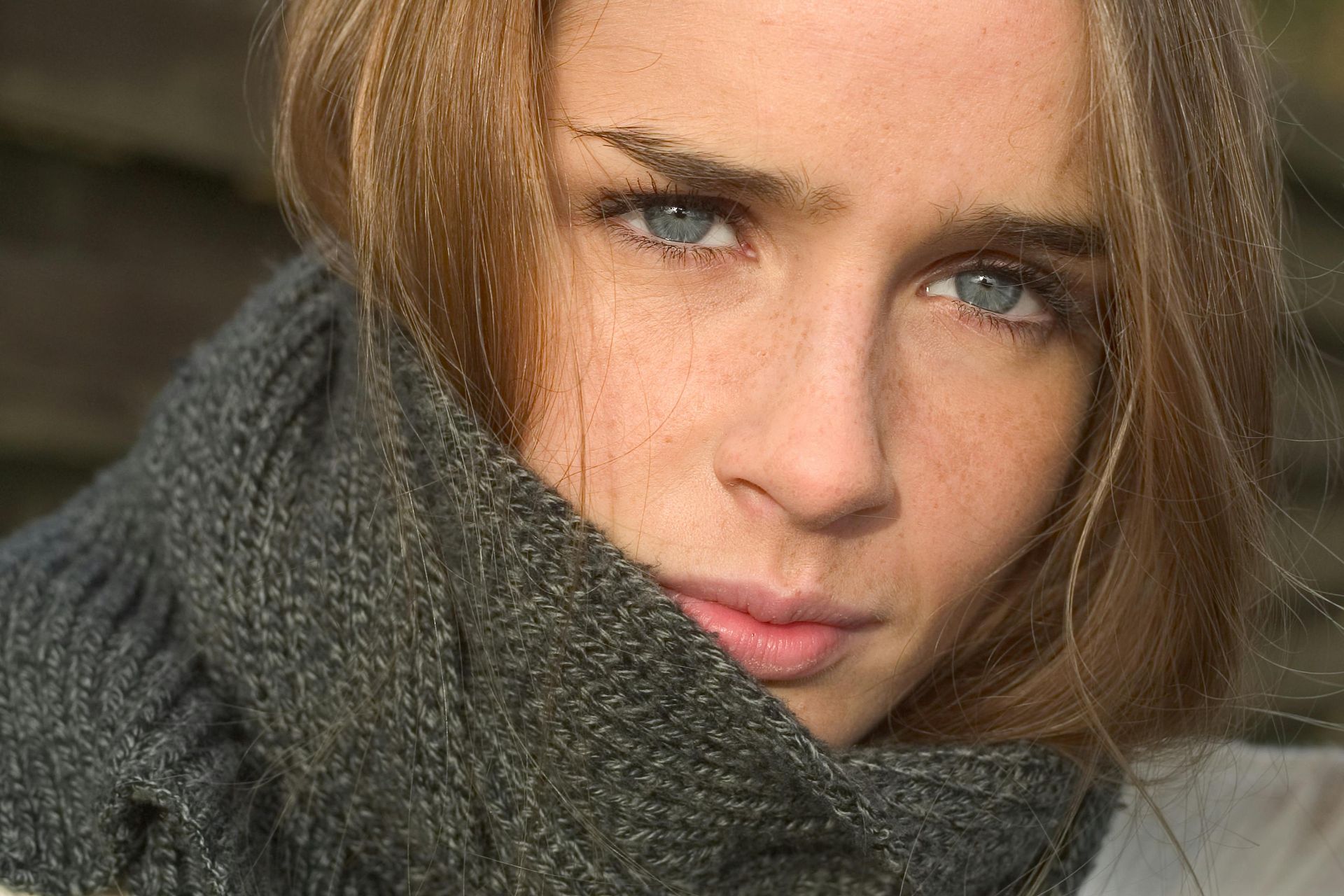 Woman with blue eyes, wrapped in a gray scarf, looking directly at the camera.