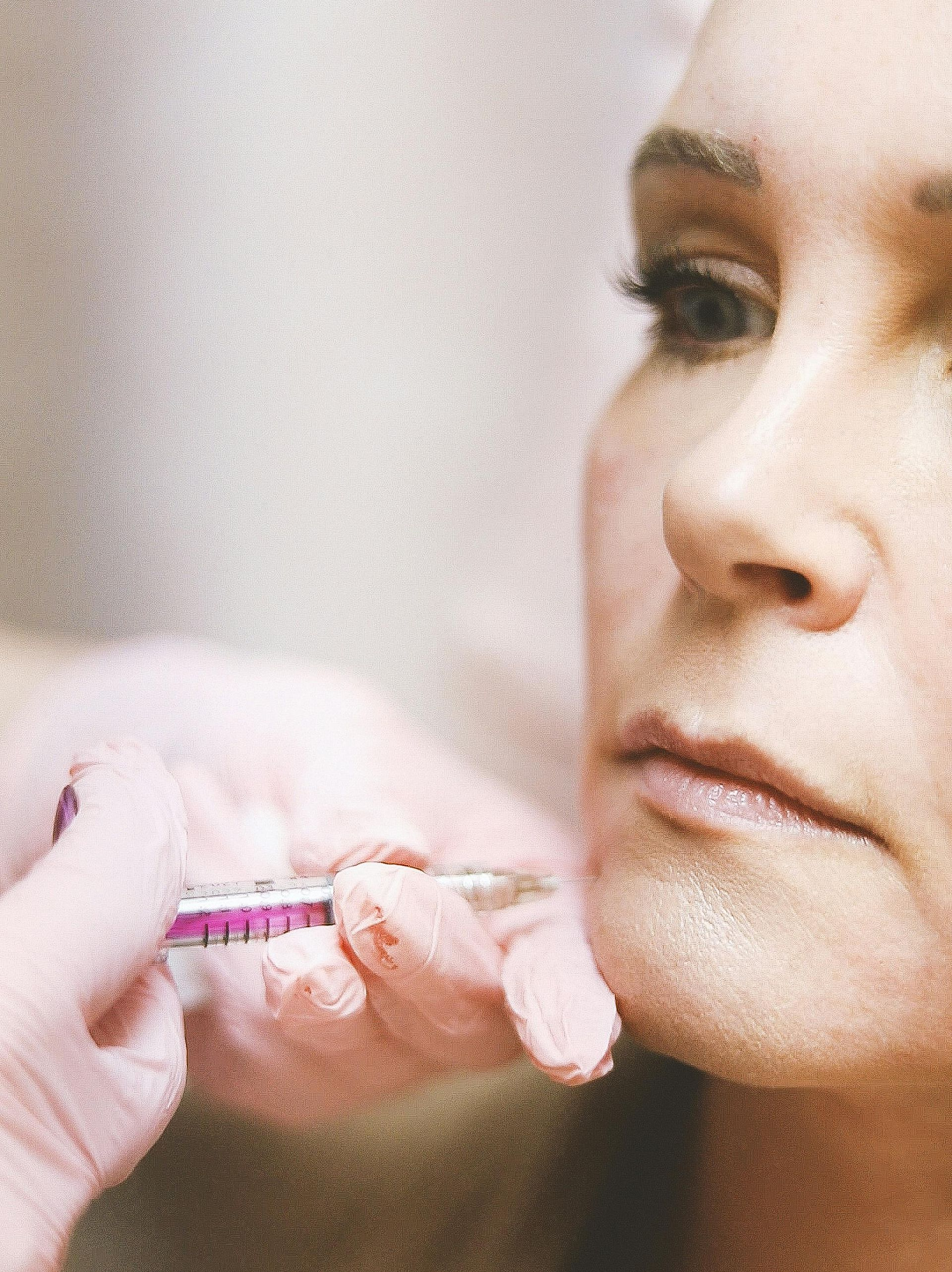 A person receives a lip injection with a syringe; close-up shows the procedure.