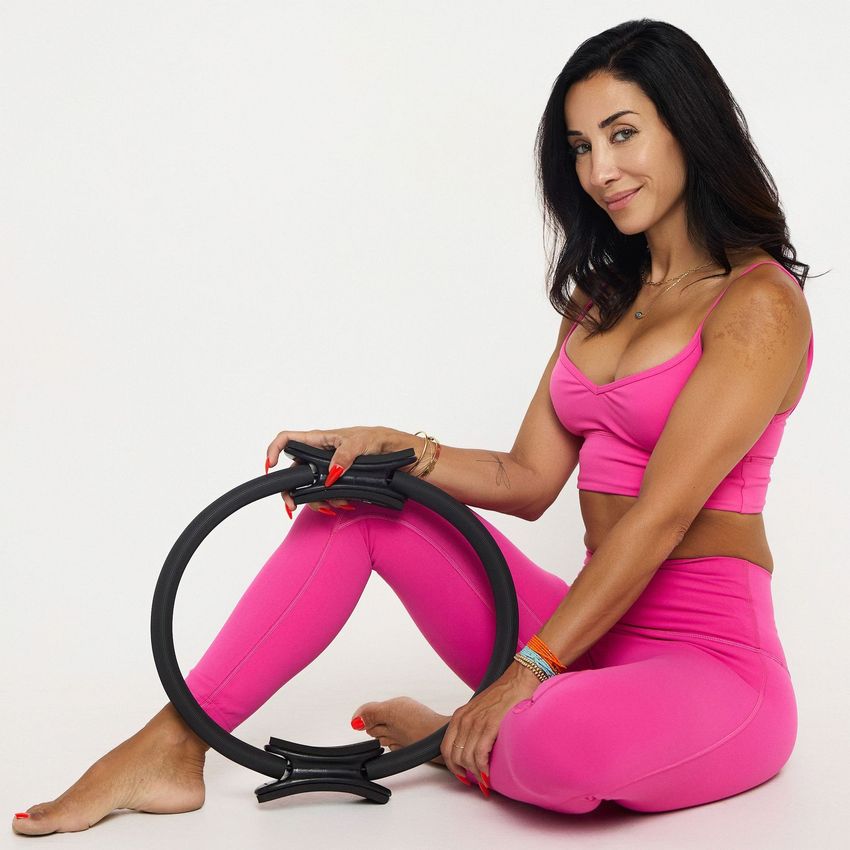 Pilates by Eve studio owner, Eve Melikian, is sitting on the floor holding a pilates ring magic circle.