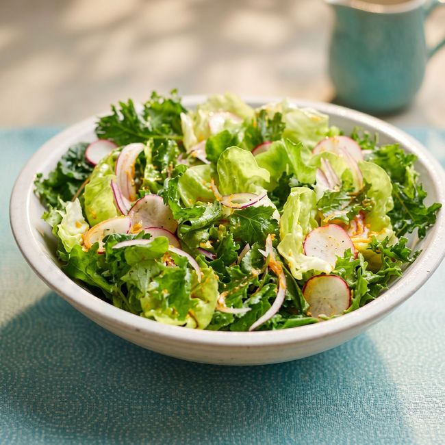 Bowl of fresh green salad with radishes on a blue tablecloth
