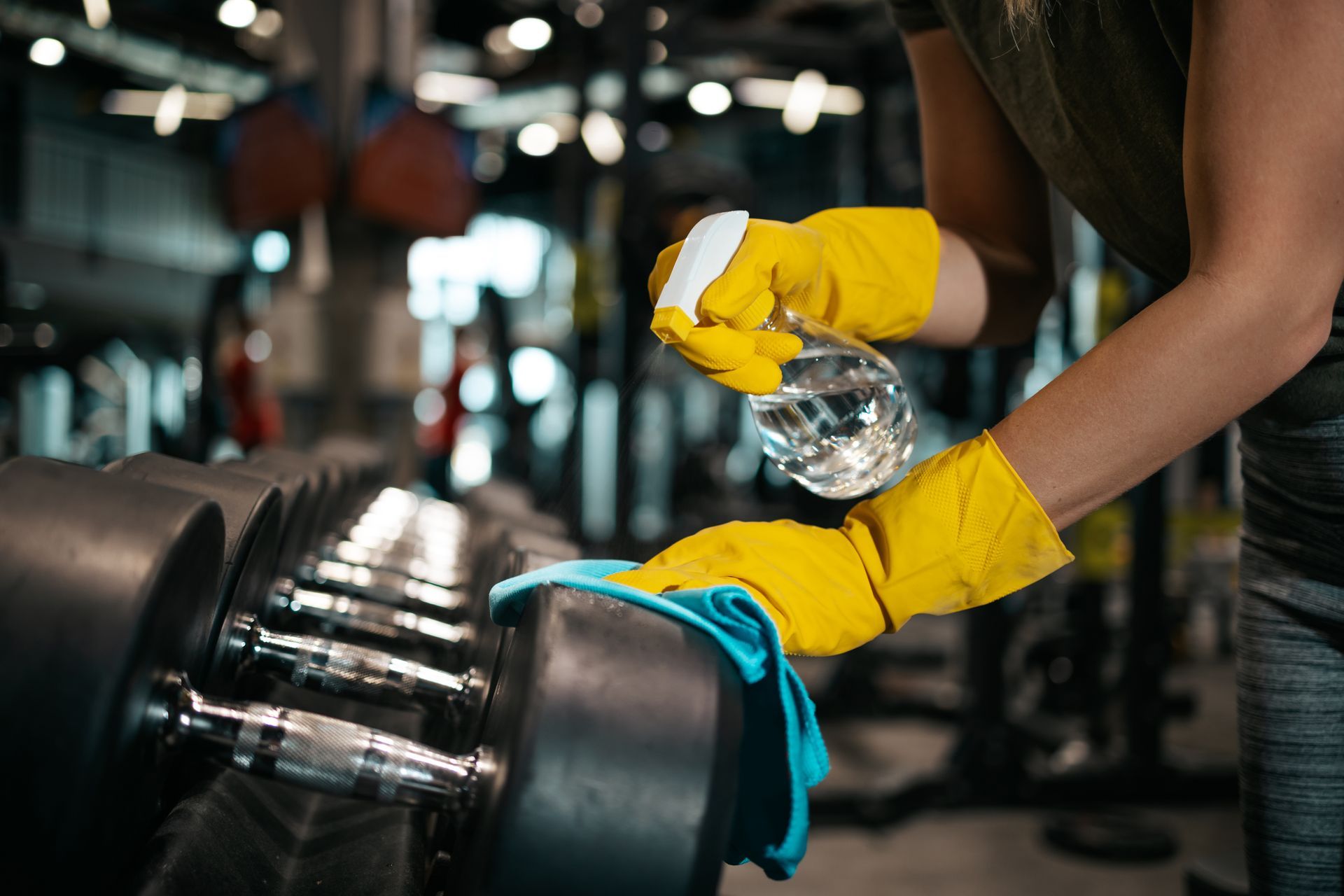Person In Yellow Gloves Wiping A Dumbbell With A Cloth In A Gym — RWM Cleaning in Deception Bay, QLD