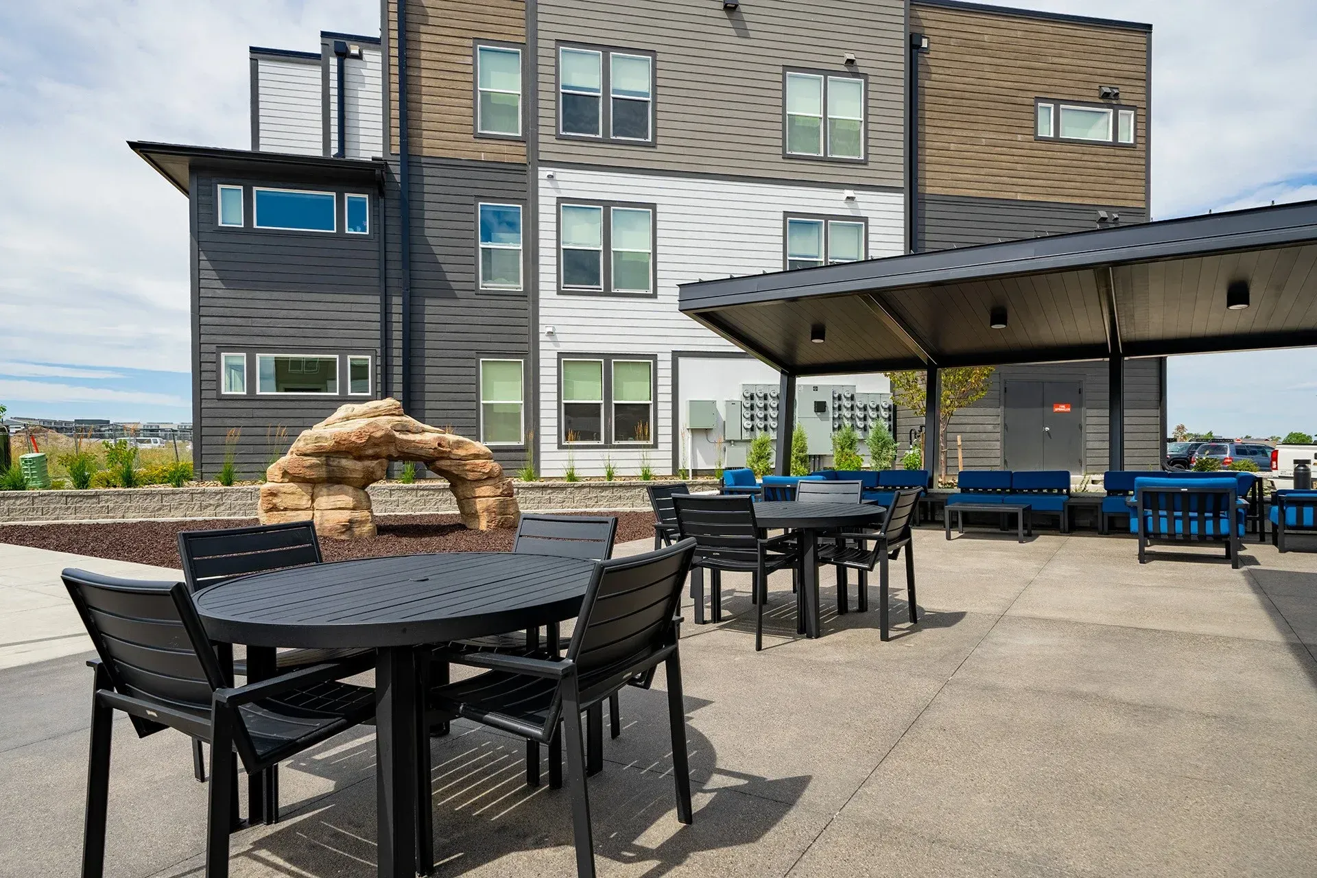 19th and Graf  Apartments Rooftop patio with black tables, chairs, and a shaded seating area; building in background.