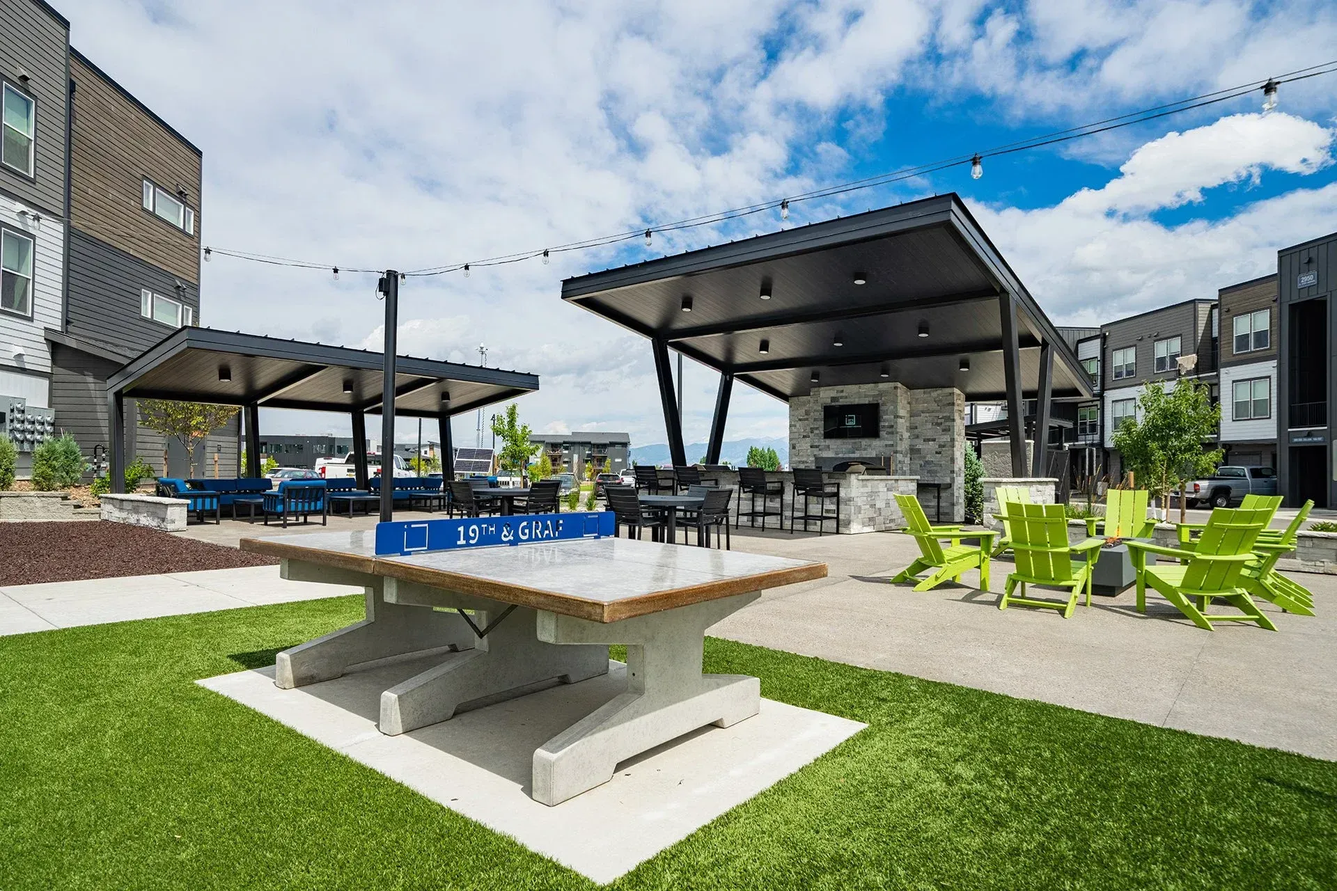 19th and Graf  Apartments Outdoor leisure area with ping pong table, lounge seating, and a fireplace under shaded structures.