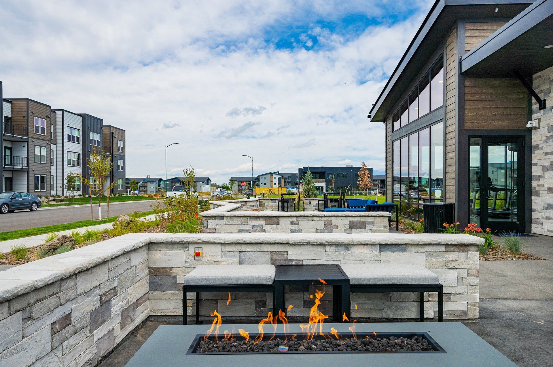 19th and Graf  Apartments Outdoor seating area with a fire pit, modern buildings in the background, cloudy sky.
