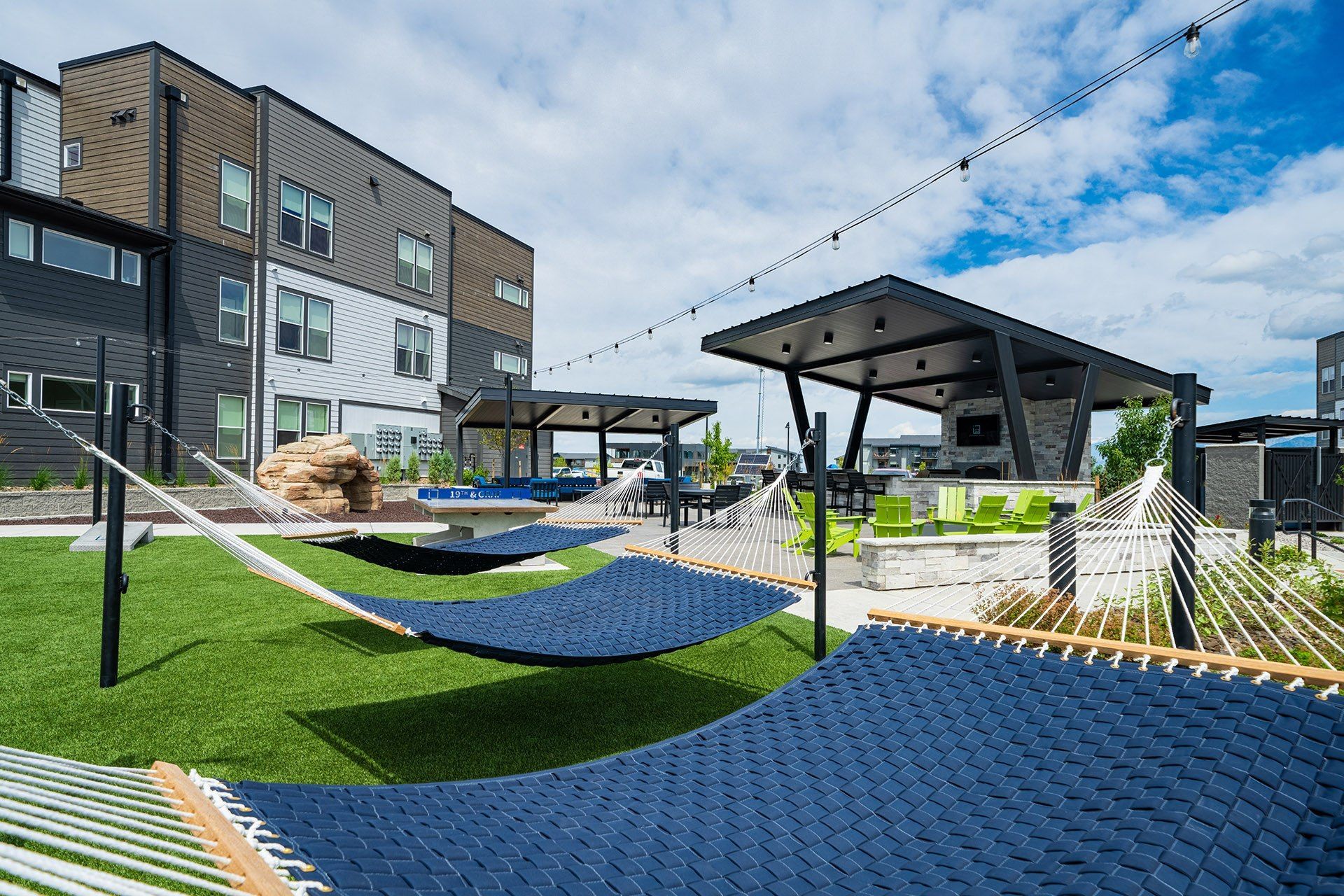 19th and Graf  Apartments Outdoor recreation area with hammocks, seating, and a modern building under a cloudy sky.