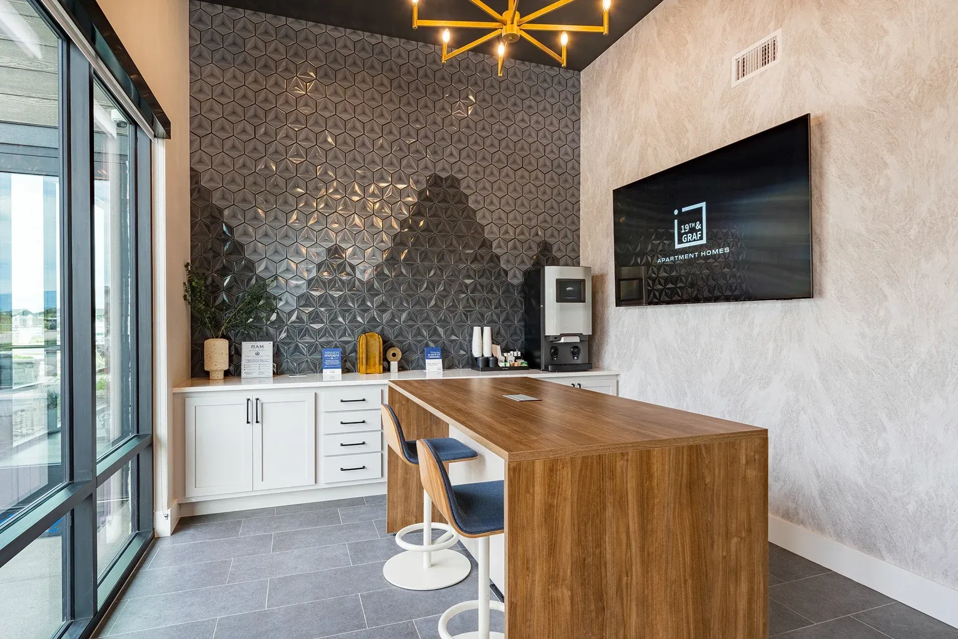 19th and Graf  Apartments Modern break room with coffee station, textured wall, and wooden island with stools.