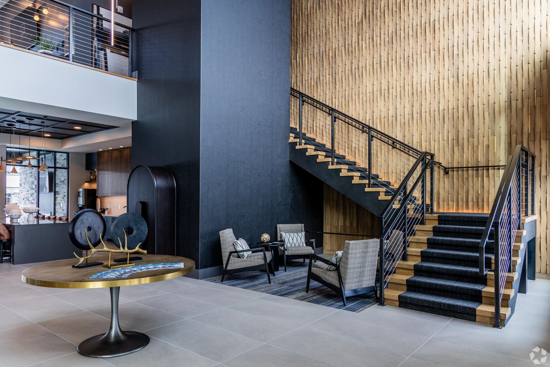 19th and Graf  Apartments Modern lobby with staircase, seating area, and decorative table. Black and wood tones.