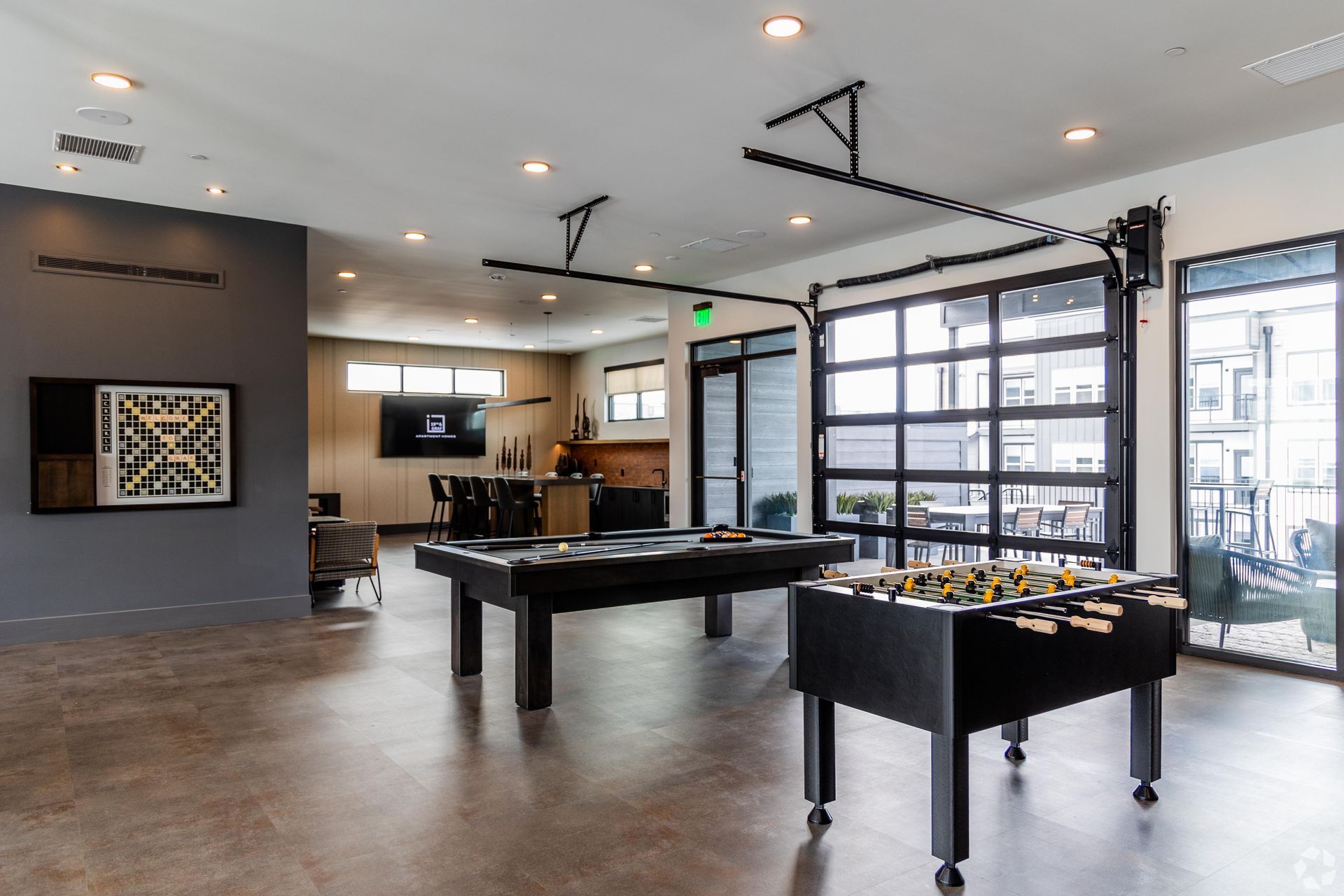19th and Graf  Apartments Game room with pool and foosball tables, dark tables and black-framed glass garage door.