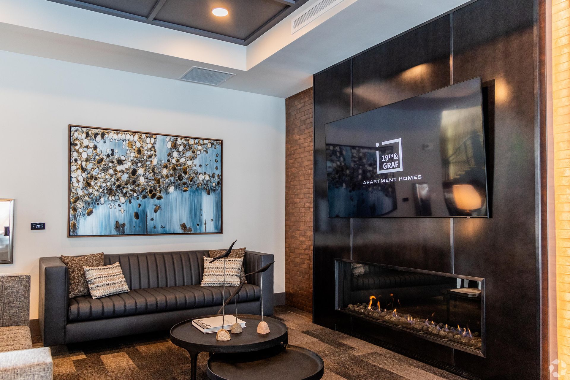19th and Graf  Apartments Lobby with a black sofa, modern fireplace, and large wall-mounted TV.