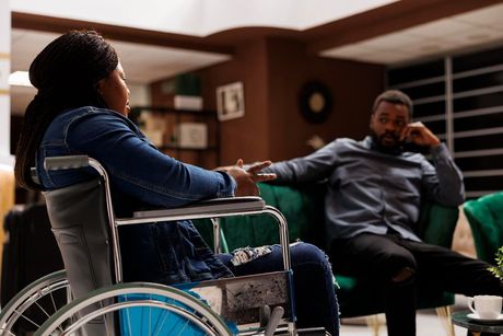 Two people sitting and talking in a living room, one in a wheelchair.