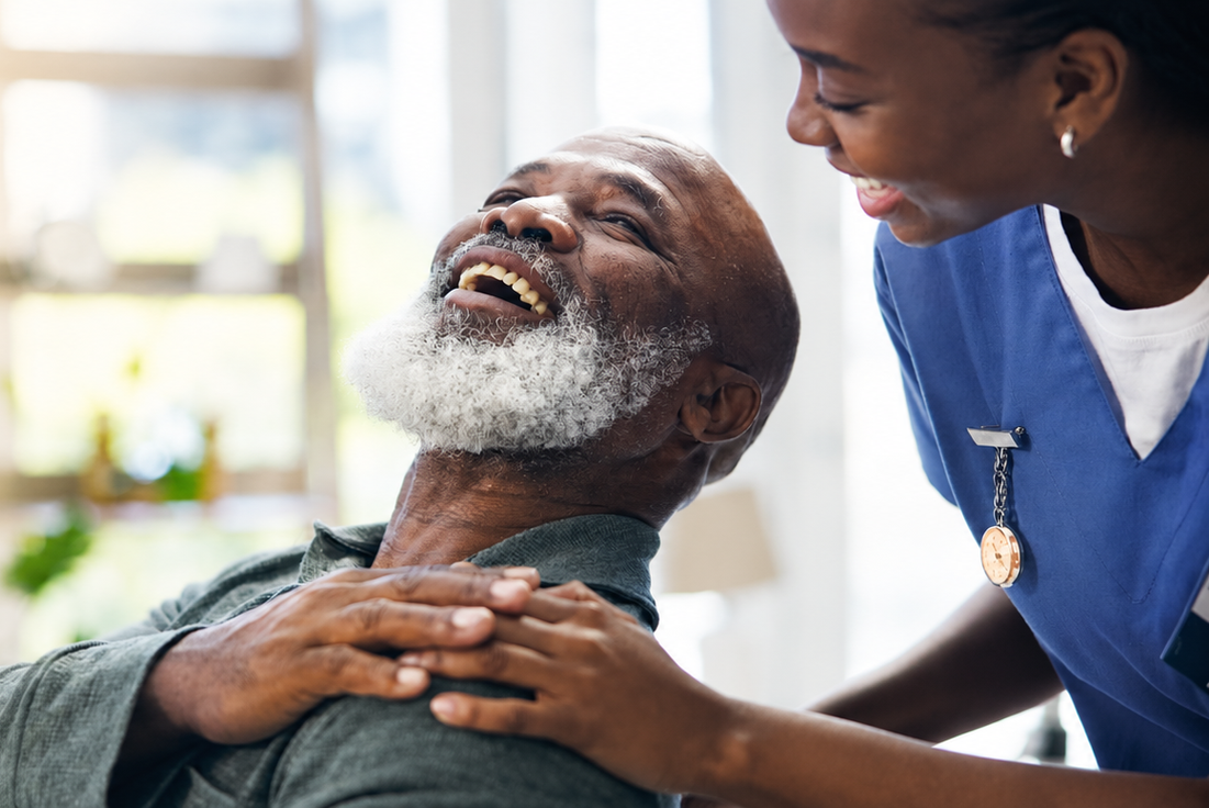 Caregiver in blue scrubs comforts a reclining patient in a bright room