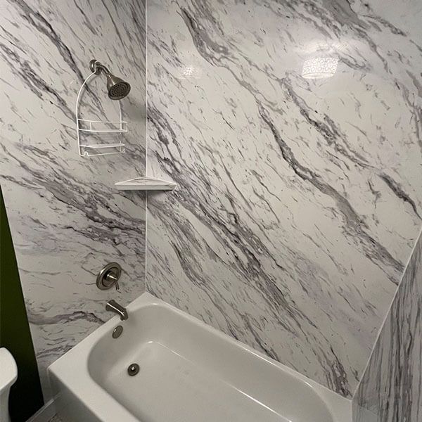 Tiled shower and bathtub corner with marble-pattern walls and chrome showerhead.