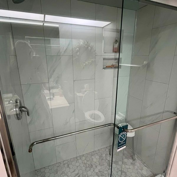 Glass shower stall with grab bars and a wall-mounted soap dispenser in a tiled bathroom