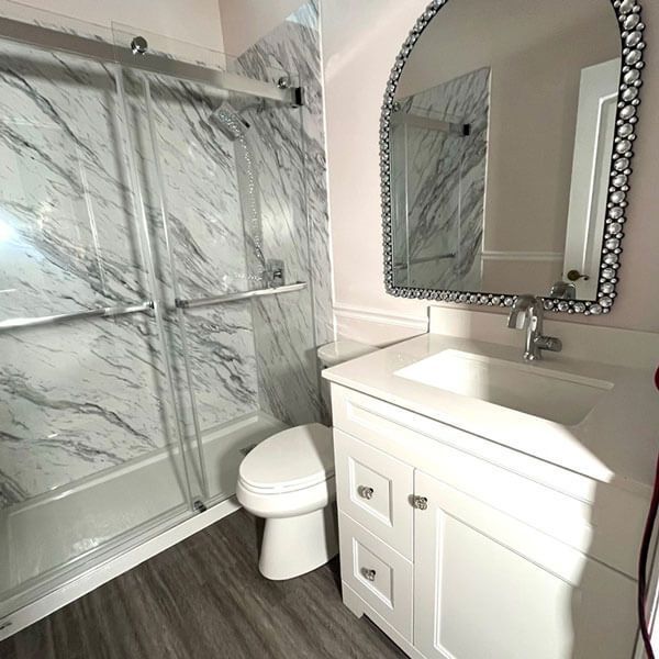 Modern bathroom with marble shower, white vanity, sink, and framed mirror