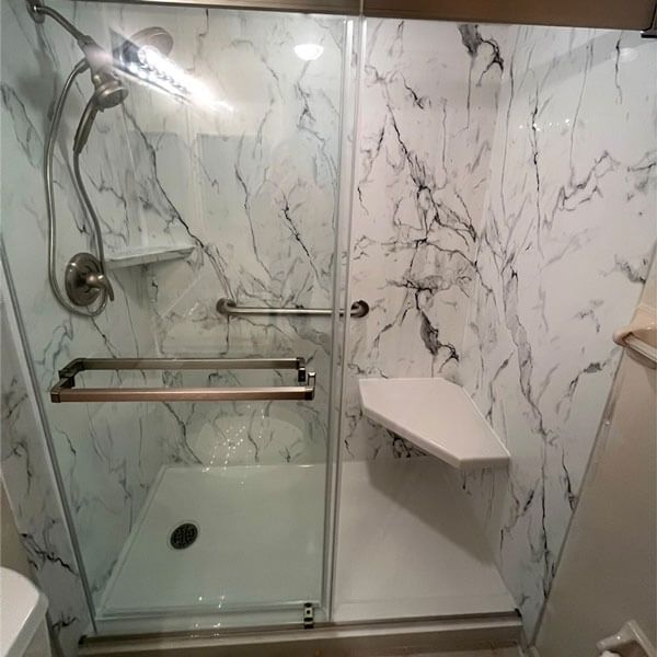 Modern tiled shower with glass door, chrome fixtures, grab bar, and built-in corner shelf