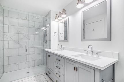 Bright white bathroom with glass shower, double vanity, and large mirror