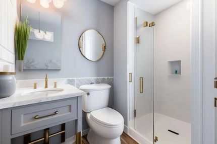 Modern white bathroom with vanity, round mirror, toilet, and glass shower.