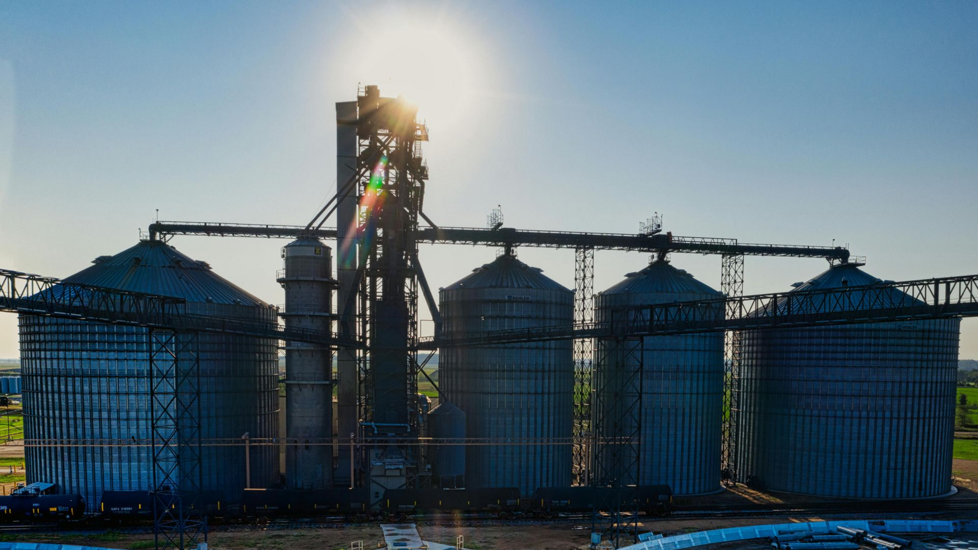 Industrial silos and equipment silhouetted against a bright sunrise at a processing plant